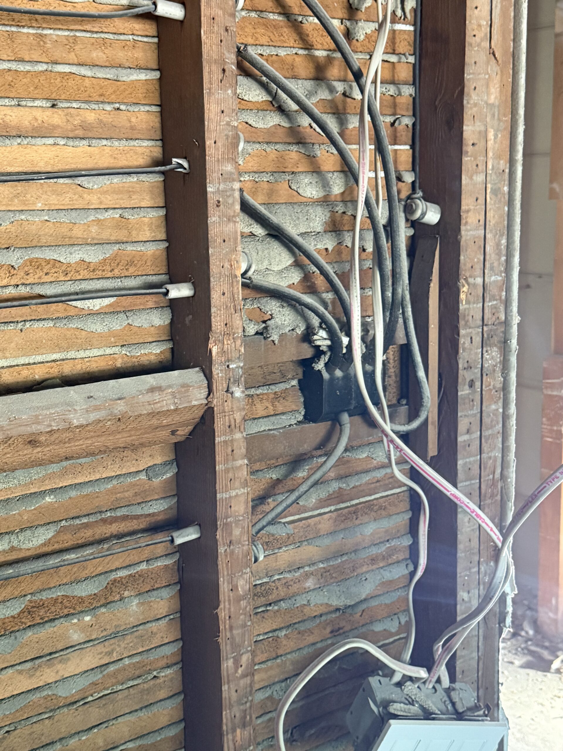 Exposed lath and plaster wall with visible electrical wiring and a disconnected electrical box.