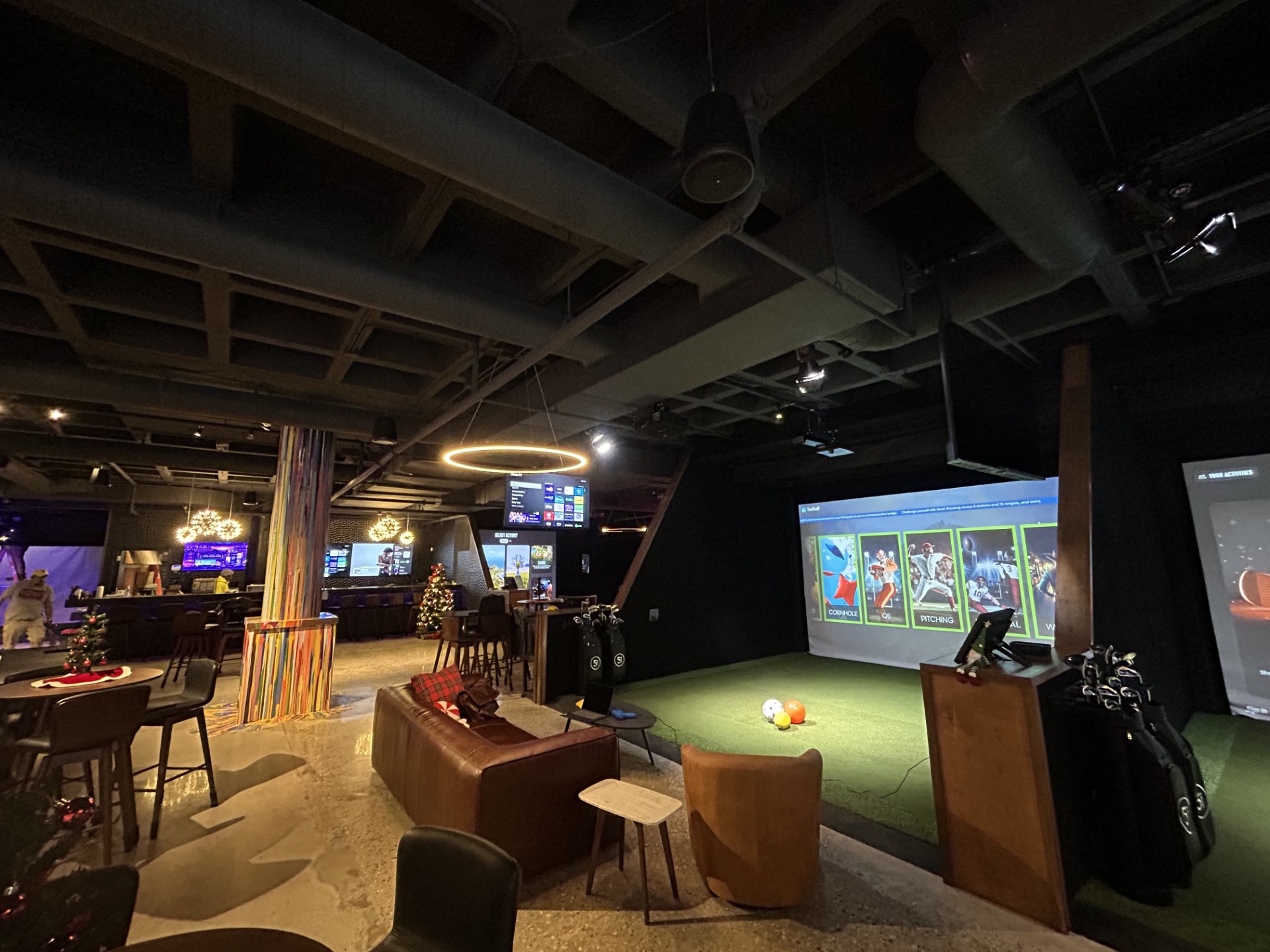 A modern indoor golf and entertainment venue featuring golf simulators, lounge seating, digital screens, festive holiday decorations, and reliable commercial electrical services for a seamless experience.